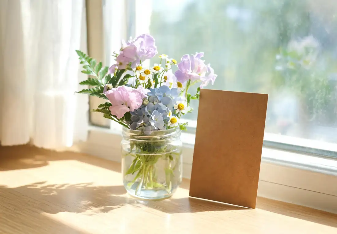 Petit bouquet de remerciement avec pois de senteur, hortensia bleu, camomille blanche et verdure dans un bocal en verre sur un rebord de fenêtre ensoleillé