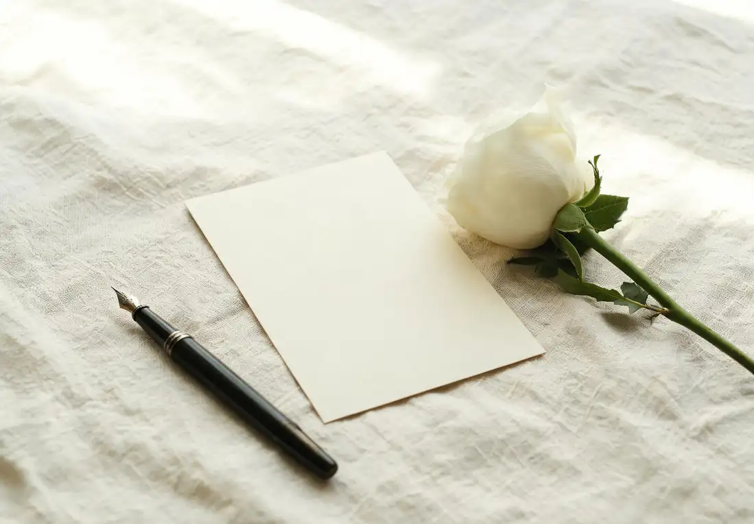 Carte de condoléances crème vierge posée sur une nappe en lin, avec un stylo à plume et une rose blanche